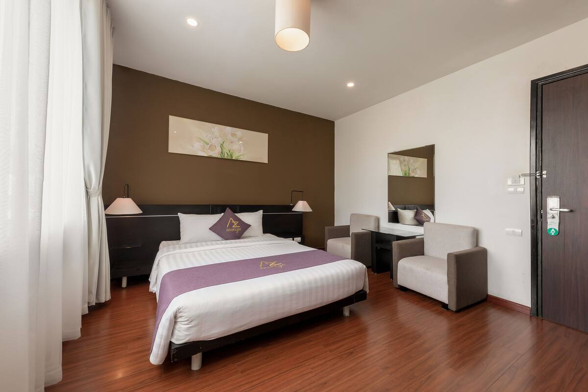 A hotel room with a bed, bedside tables, a desk, a chair, and a wardrobe.