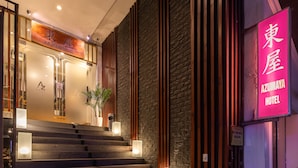 Entrada de un hotel con una escalera que lleva al vestíbulo, un letrero de neón y una pared de piedra.