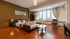 Una habitación de hotel moderna con un sofá, una mesa de centro de vidrio, un escritorio y un ventanal con cortinas.