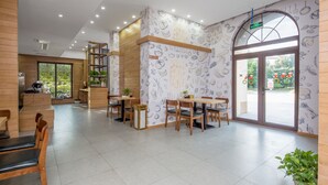 Un café moderne, avec un intérieur décoré de meubles en bois, un espace salon central et un mur orné d’illustrations représentant des aliments.