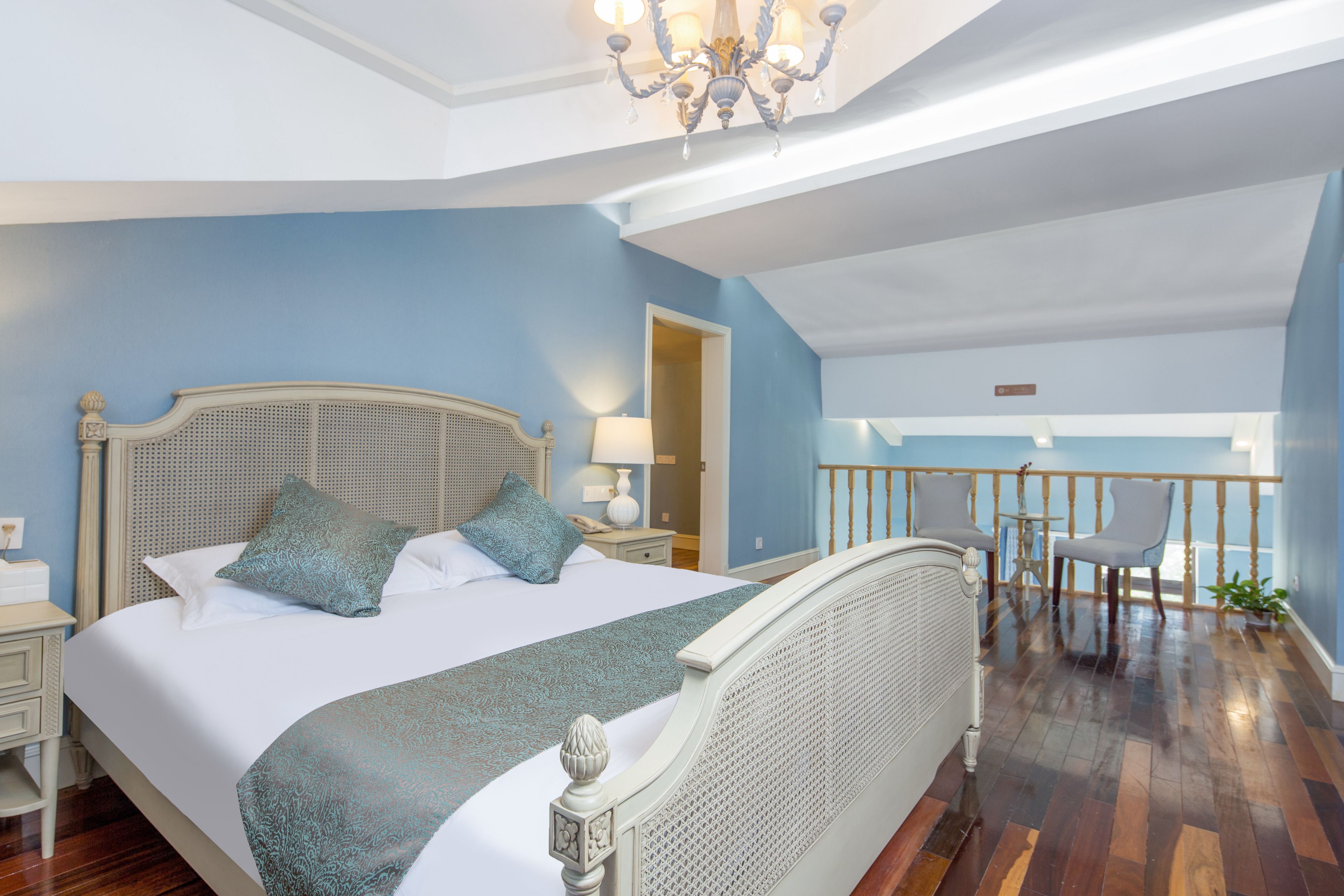 Quarto com uma cama grande, um candelabro, uma varanda com cadeiras e vista para o exterior.
