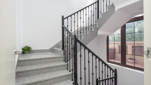 Un escalier avec des marches en granit et des balustrades noires, menant à un palier d’où l’on peut admirer un jardin.