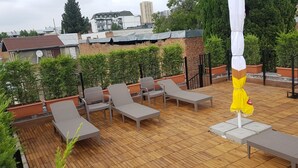 Une terrasse sur le toit, avec des chaises longues, un parasol jaune et des plantes en pot.