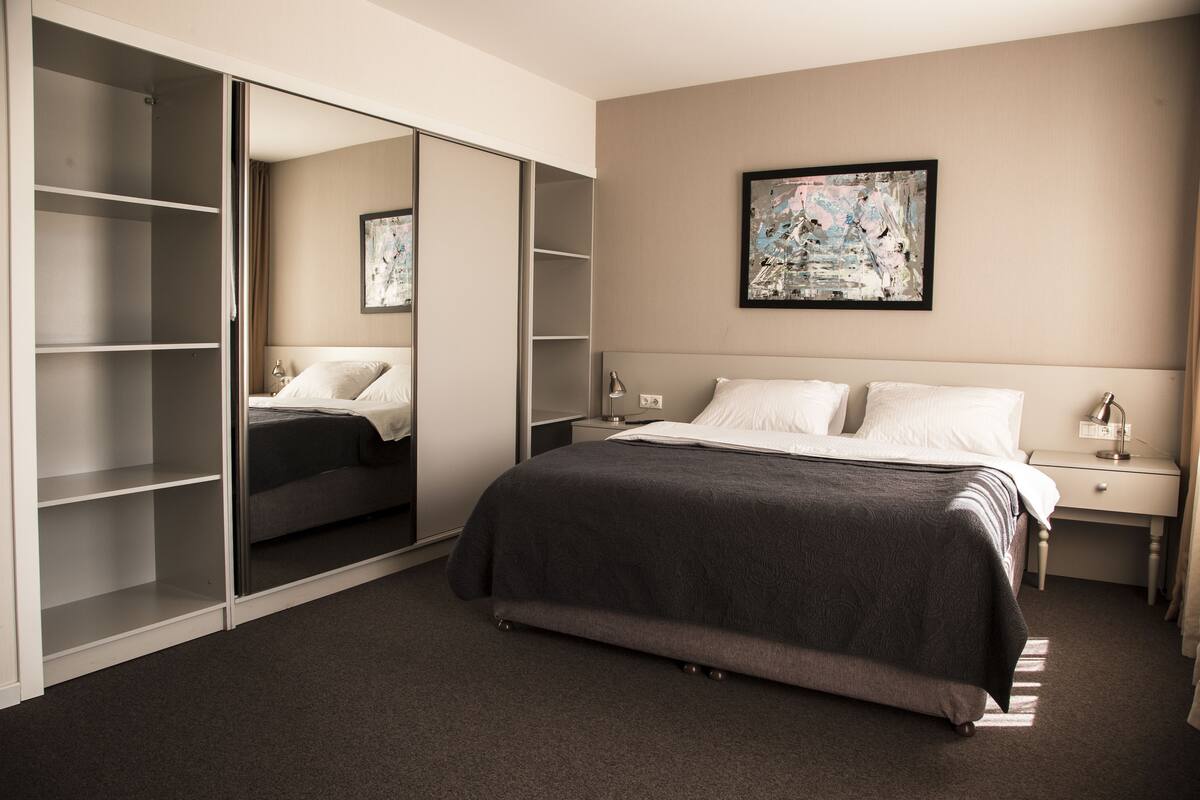 A bedroom with a bed, a nightstand, a bedside table, a wardrobe, and a painting on the wall.
