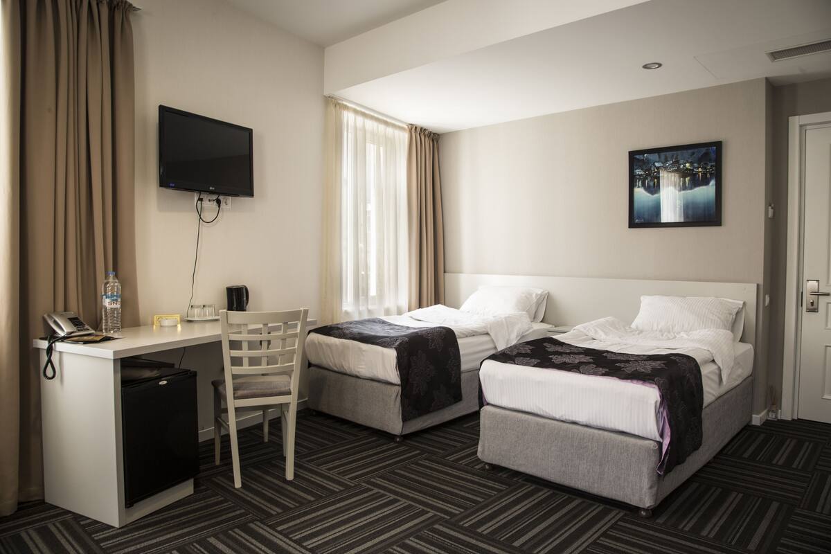 A hotel room with two beds, a desk, a TV, and a small refrigerator.