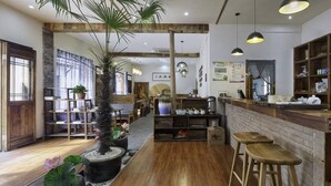 Ein gemütliches Café mit Holzdielen, einer zentral platzierten Pflanze und einer Bar mit Hockern.