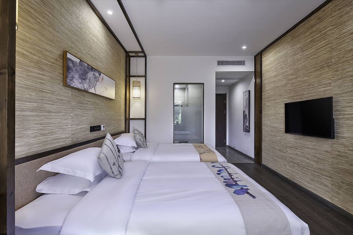 Ein modernes Hotelzimmer mit zwei Betten, einem Flachbildfernseher und einem großen Fenster.