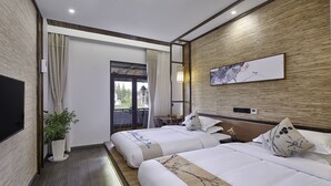 Ein Hotelzimmer mit zwei Betten, einem Flachbildfernseher, einer Topfpflanze und einem großen Fenster mit Vorhängen.