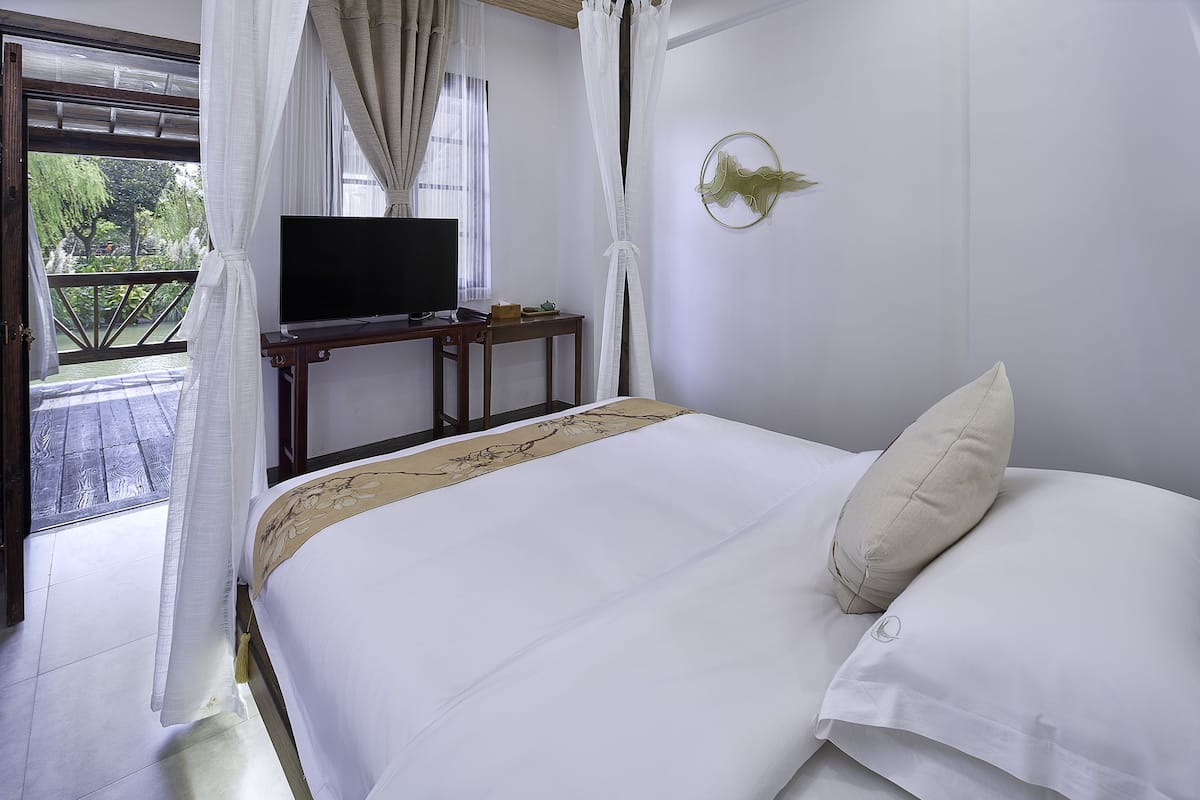 Ein Hotelzimmer mit einem Bett, einem Fernseher auf einem Holztisch und Blick auf Grünflächen.