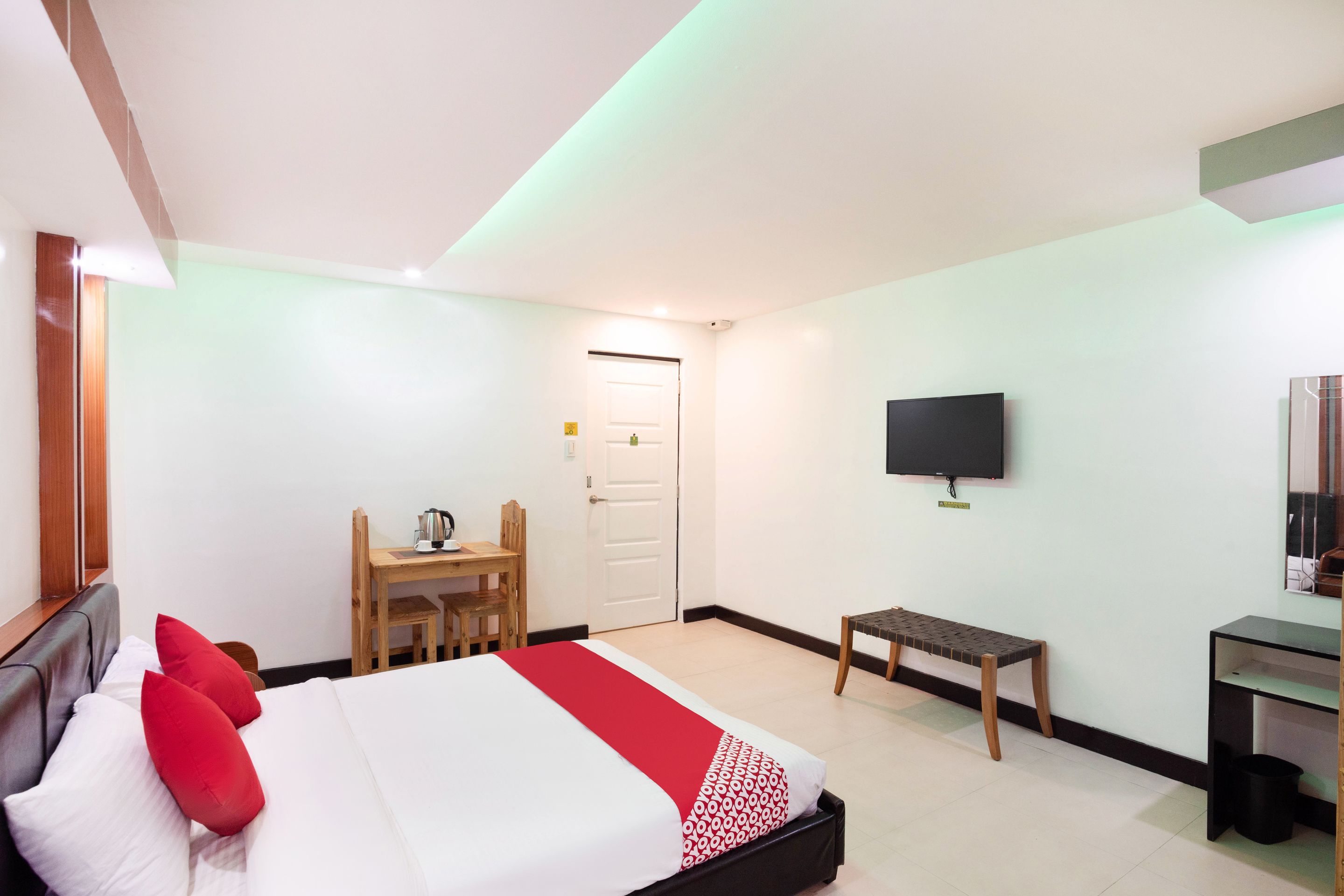 Una habitación de hotel con cama, escritorio, silla, televisor y una banca.