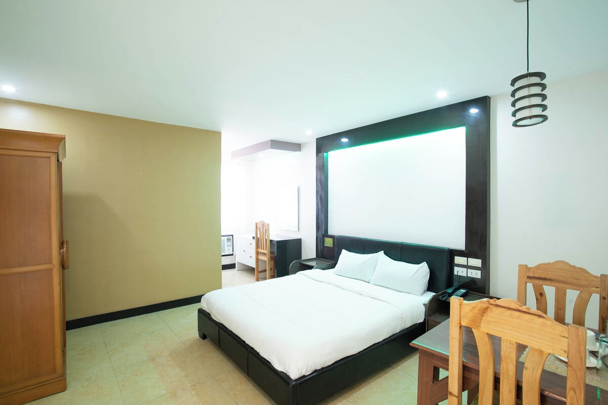 A hotel room with a bed, a desk, a chair, a wardrobe, and a large window.