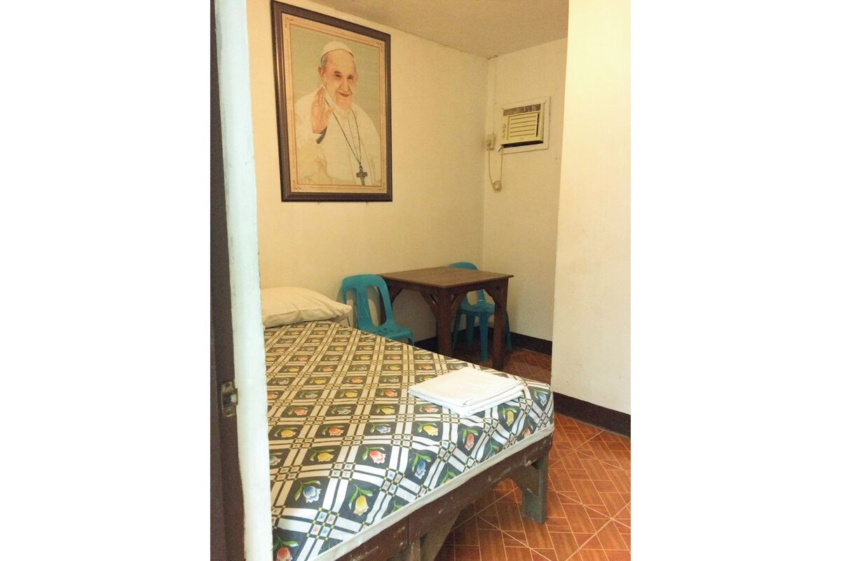 Una habitación con cama, escritorio, dos sillas, un cuadro en la pared y un aire acondicionado instalado en la pared.