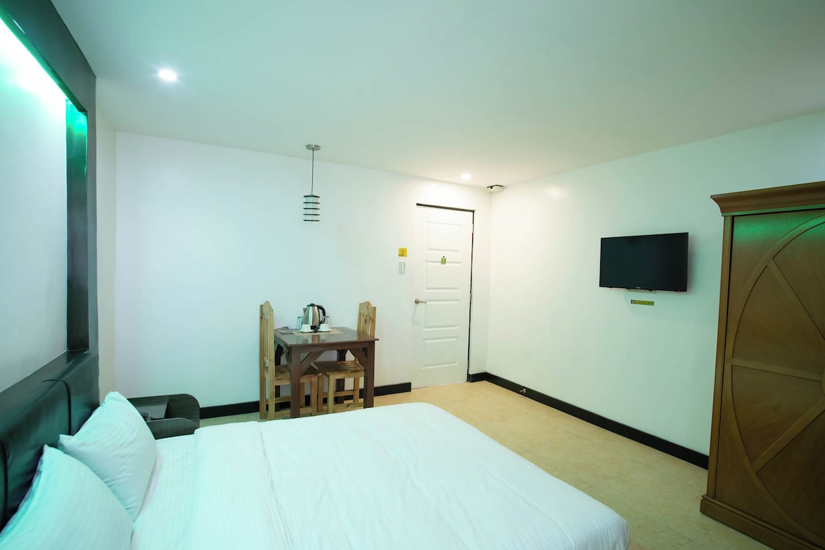 A hotel room with a bed, a desk with a chair, a television, and a wardrobe.