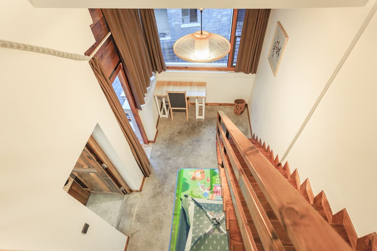 A high-angle view of a staircase with wooden railings, a small table with chairs, and a window with curtains.