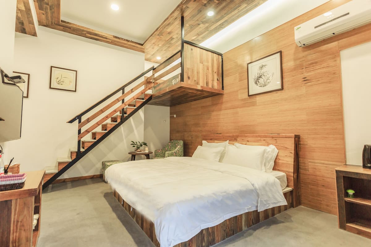 A bedroom with a wooden bed, a staircase with a wooden railing, and a wall-mounted air conditioner.
