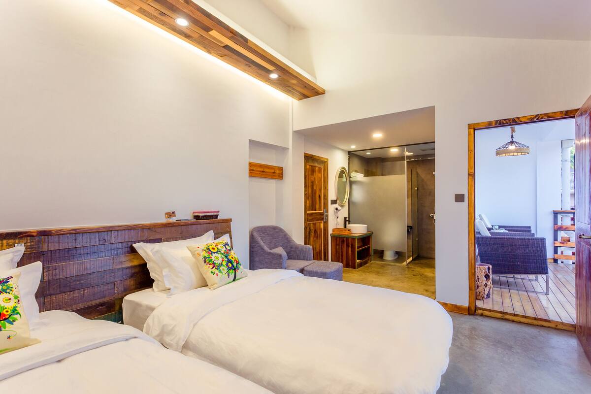 A bedroom with two beds, a wooden headboard, a chair, a small table, and a mirror.