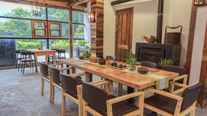 A wooden dining table with chairs, a fireplace, and a large window overlooking greenery. - That Mountain That Shed (Huzhou)