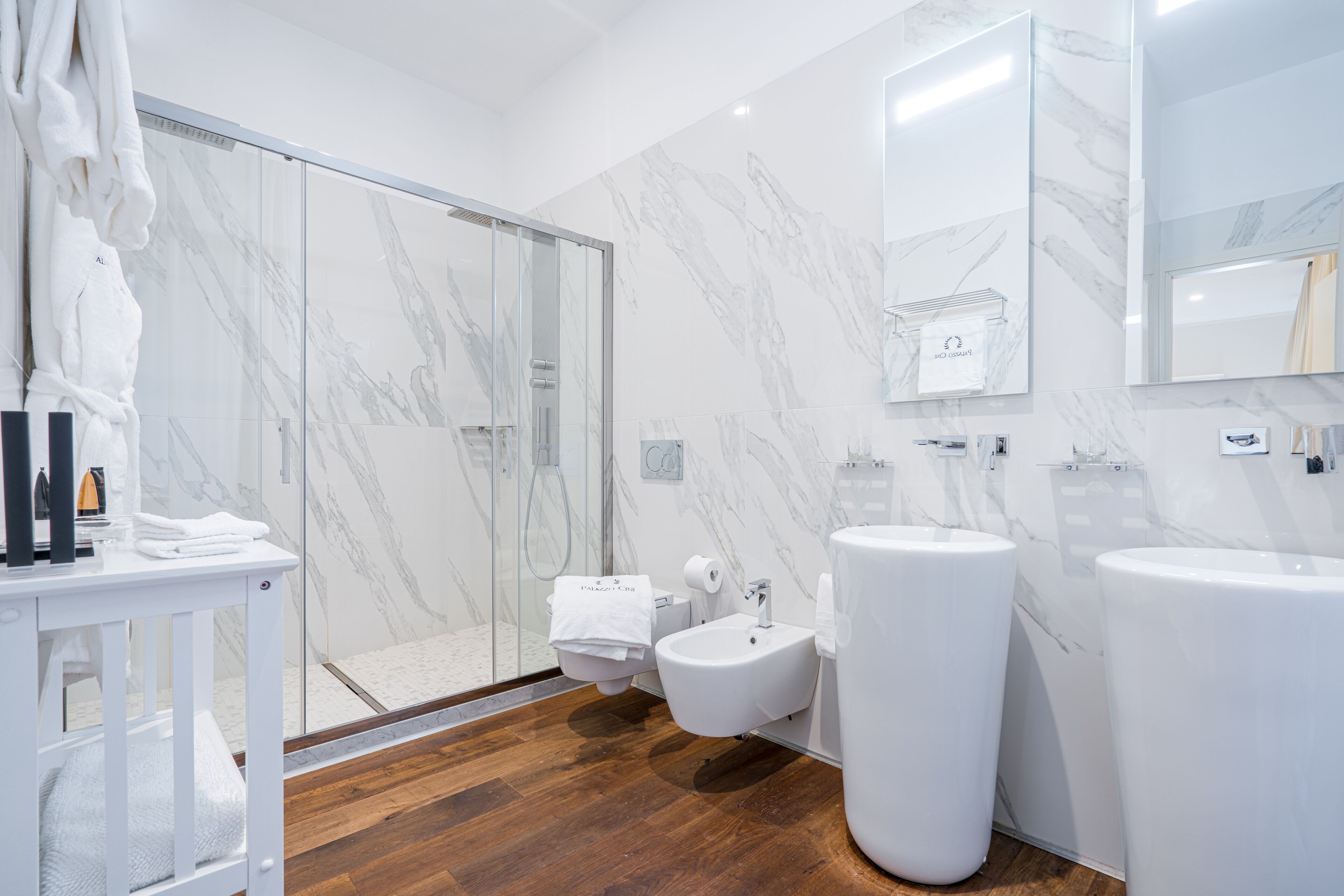 A modern bathroom with a glass shower enclosure, a bidet, and two large sinks.