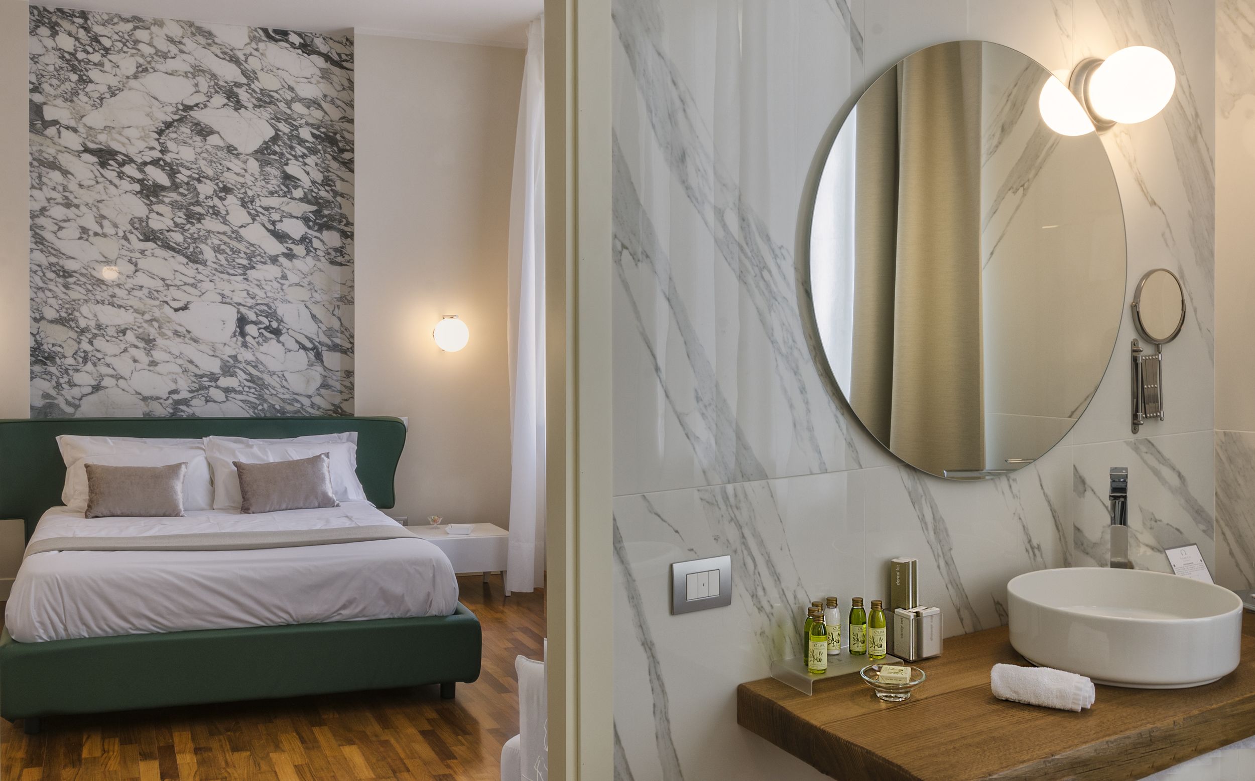 A modern hotel room with a marble wall, a green bed, a round mirror, and a wooden vanity with toiletries.