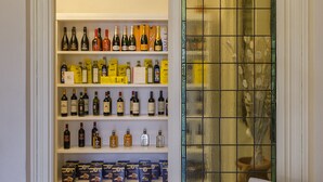 A wine cellar with shelves of wine bottles and boxes, a white cushioned bench, and a stained glass window. - Palazzo Cini Luxury Rooms In Pisa (Pisa)