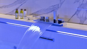 A marble wall with a blue-lit sink and three olive oil bottles. - Palazzo Cini Luxury Rooms In Pisa (Pisa)