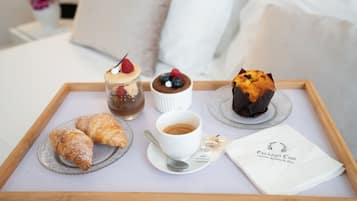 Un vassoio con pasticcini, una tazza di caffè e un dolce su un letto con lenzuola bianche.