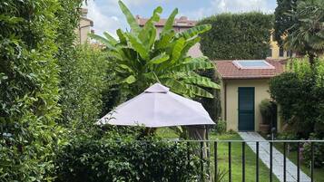 Un patio con suelo de baldosas, una pérgola con un paraguas blanco y diversas plantas en macetas.