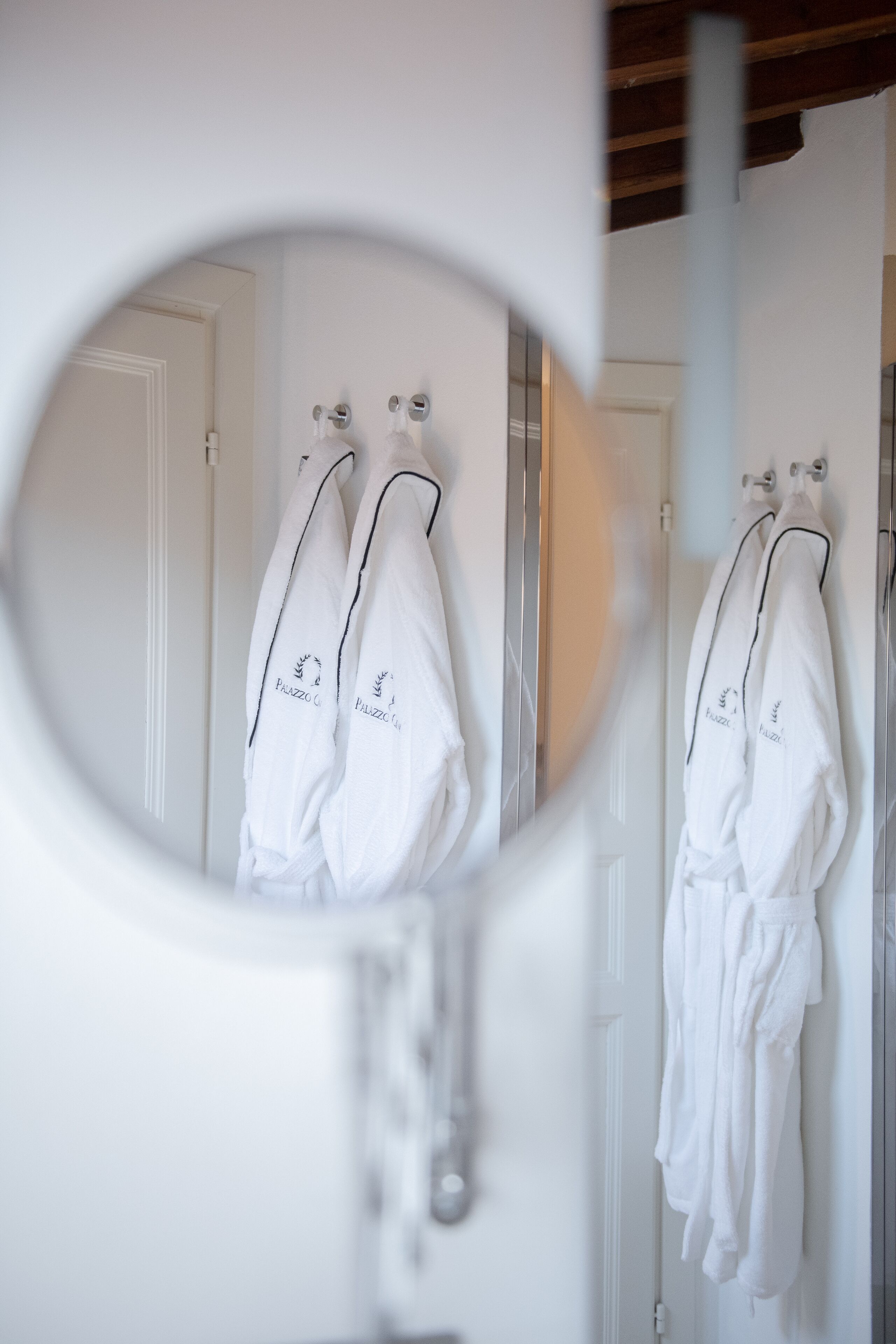 Un baño con toallas blancas colgadas en ganchos y un espejo que refleja la habitación.