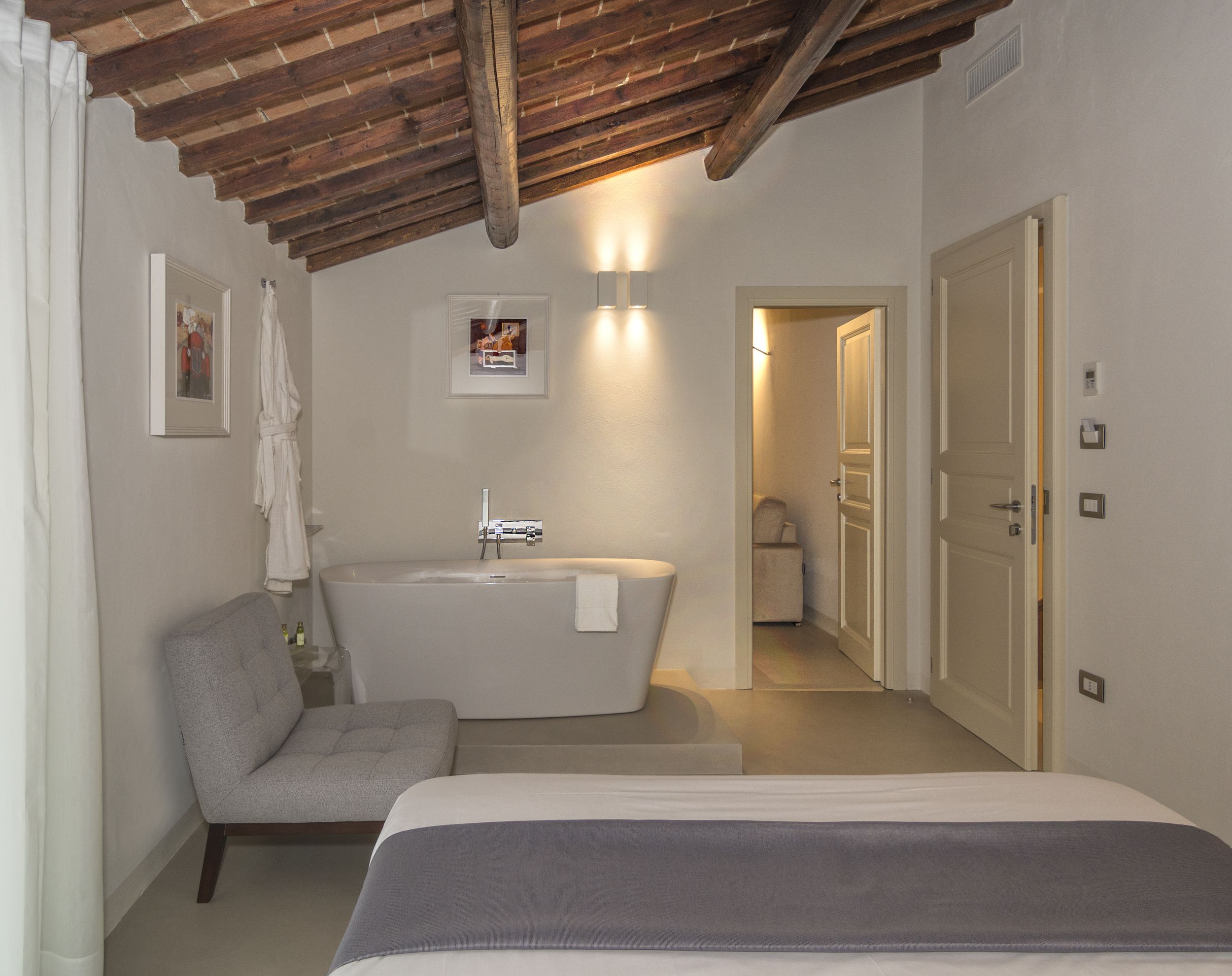Una camera da letto con un letto, una poltrona grigia, una vasca da bagno e una porta che dà su un corridoio.