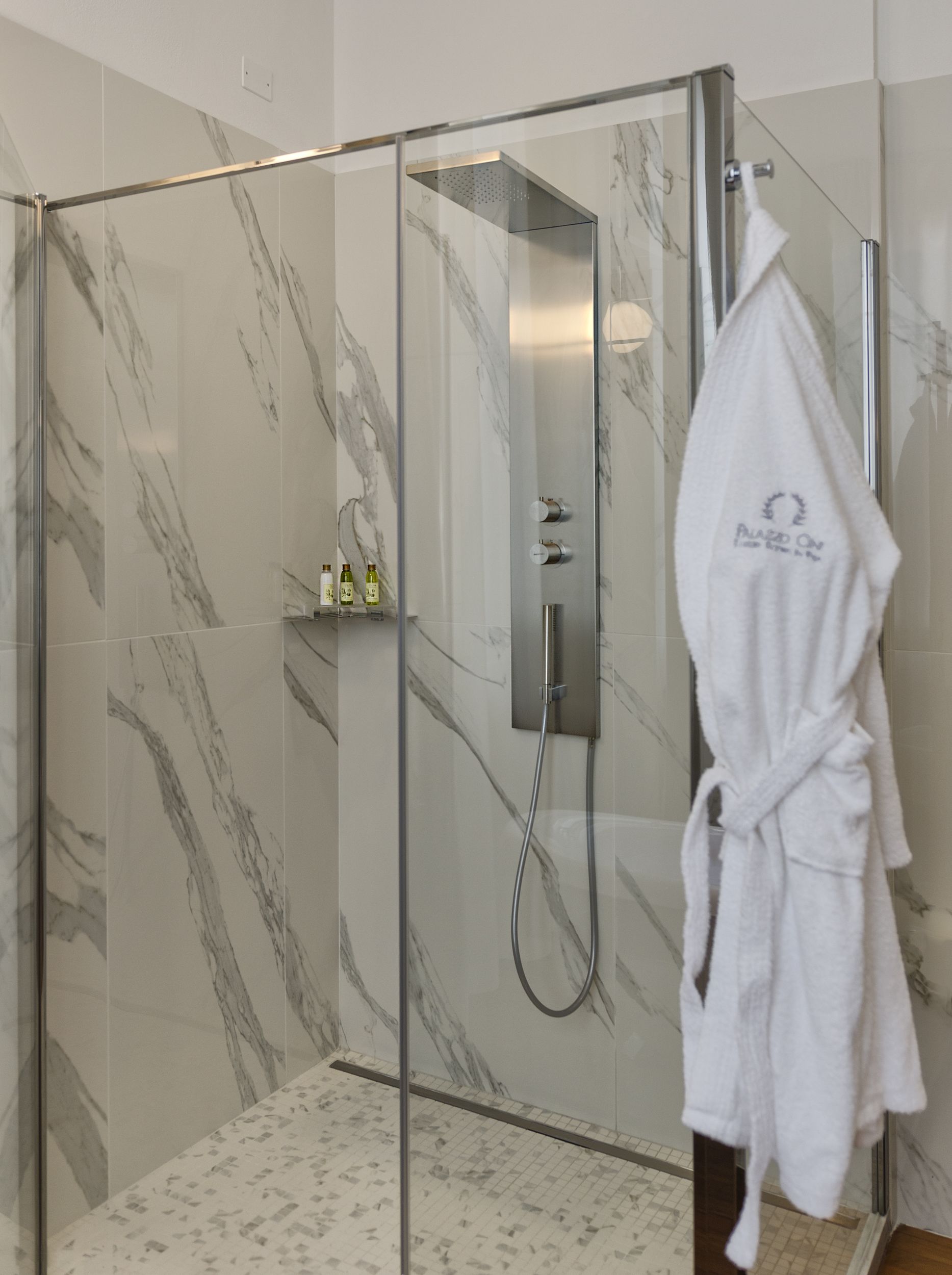 A glass-enclosed shower with a handheld showerhead, a towel rack with a robe, and marble-patterned walls.