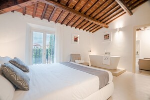 Un dormitorio con una cama grande, un baño con bañera y un balcón con vistas.