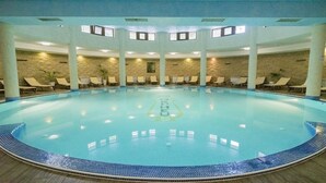 Una amplia piscina interior con borde de azulejos, rodeada de sillones de descanso y un muro de piedra.