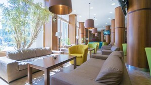 Un vestíbulo moderno con zonas de estar, ventanas amplias y una pantalla de televisión.