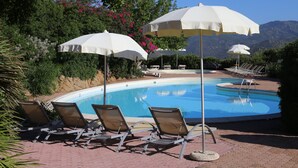A swimming pool with lounge chairs and umbrellas, surrounded by greenery and mountains.