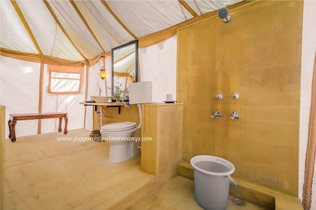 A compact bathroom with a toilet, sink, and shower area, featuring a wooden door and a small bench.