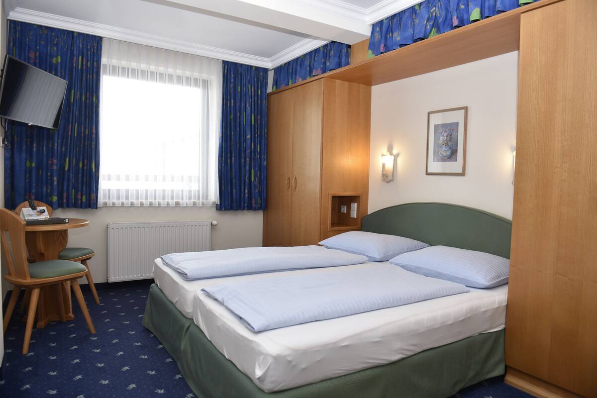A hotel room with two beds, a desk with a chair, a television, and a window with curtains.