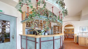 A bar area with a curved counter, shelves with glassware, and a hanging plant decoration. - Hotel Skischule Krallinger (Tweng)