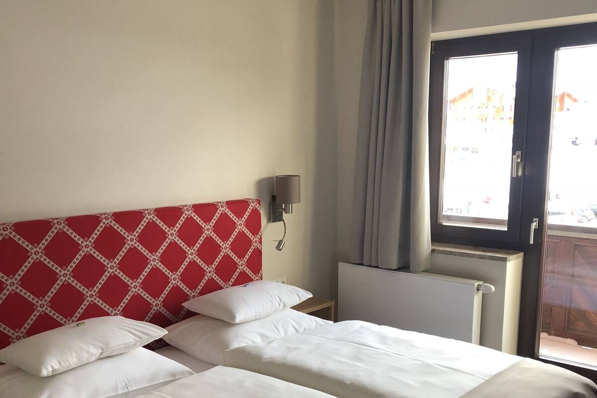 A hotel room with a bed, a nightstand, a lamp, and a window with curtains.