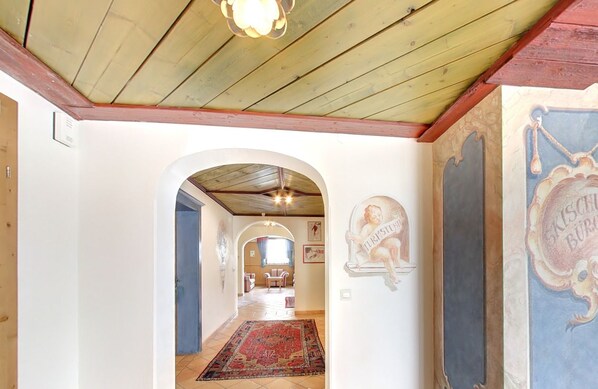 A hallway with a wooden ceiling, an arched doorway, a red patterned rug, and a wall with a decorative emblem.