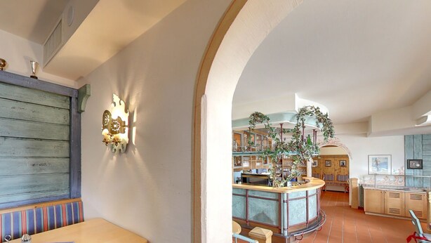 A bar area with a counter, seating, and a view of the kitchen area. - Hotel Skischule Krallinger (Tweng)