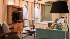 Habitación de hotel con cama, sofá, televisión, lámpara y ventana con cortinas.