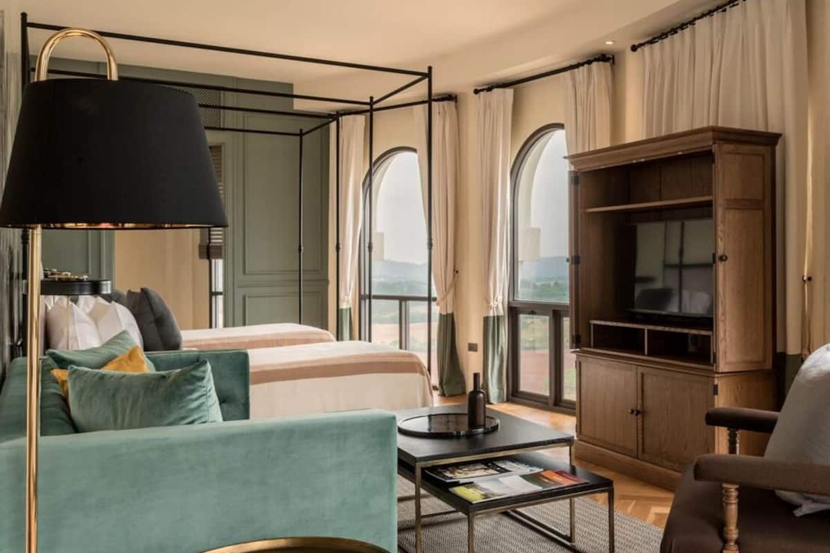 A modern hotel room with a large bed, a sofa, a coffee table, and a TV cabinet.