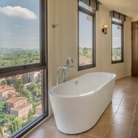 Un baño amplio con una bañera independiente, ventanas grandes que ofrecen vistas a un pueblo, y una puerta de madera.