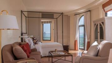 Una habitación de hotel moderna con una cama grande, una zona de estar con sofá y sillones, una mesita y un ventanal con vistas.