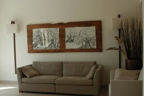 Ein Wohnzimmer mit einem beigefarbenen Sofa, einem großen abstrakten Gemälde an der Wand, einer Stehlampe und einer hohen Vase mit Zweigen.