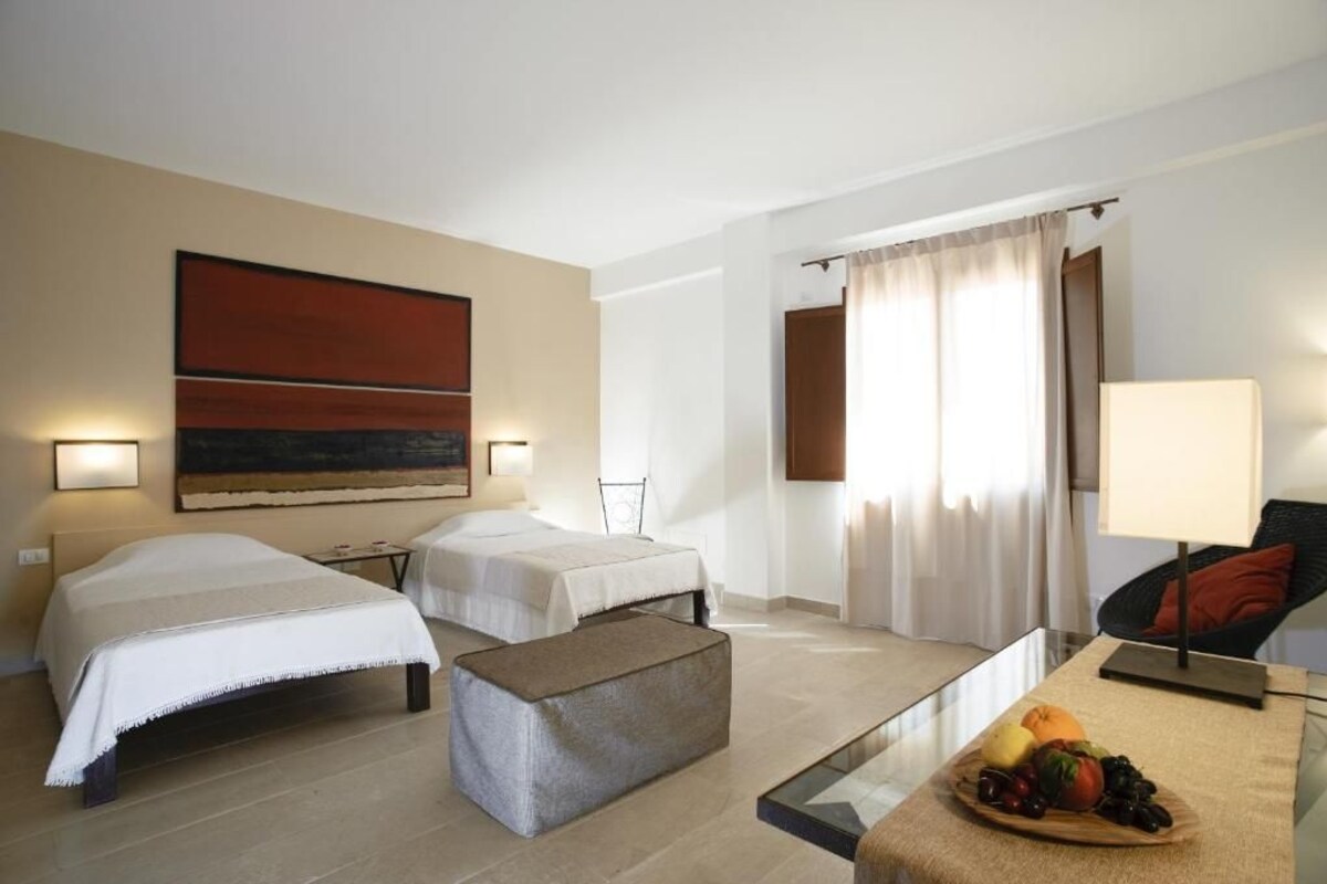 A hotel room with two beds, a sofa, a glass coffee table with fruit, and a painting on the wall.