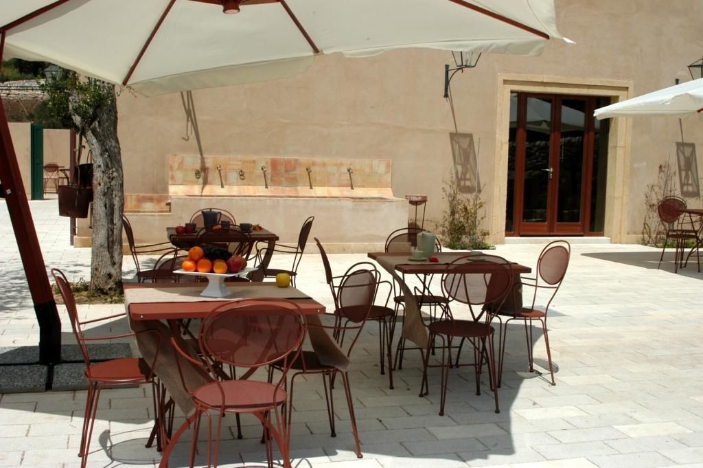 Un área de comedor al aire libre con mesas y sillas, un frutero y un paraguas grande.