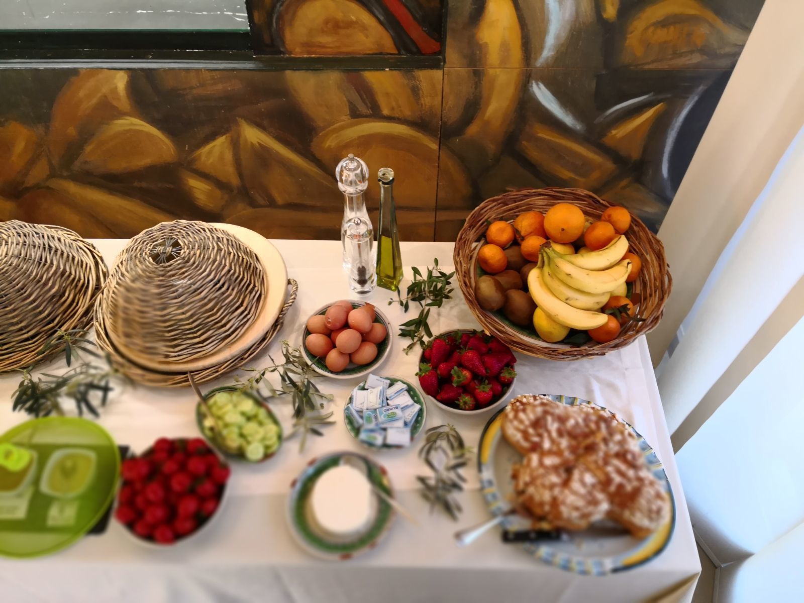 A table with various food items and condiments, including baskets of fruits, bowls of eggs, and a plate of pastries.