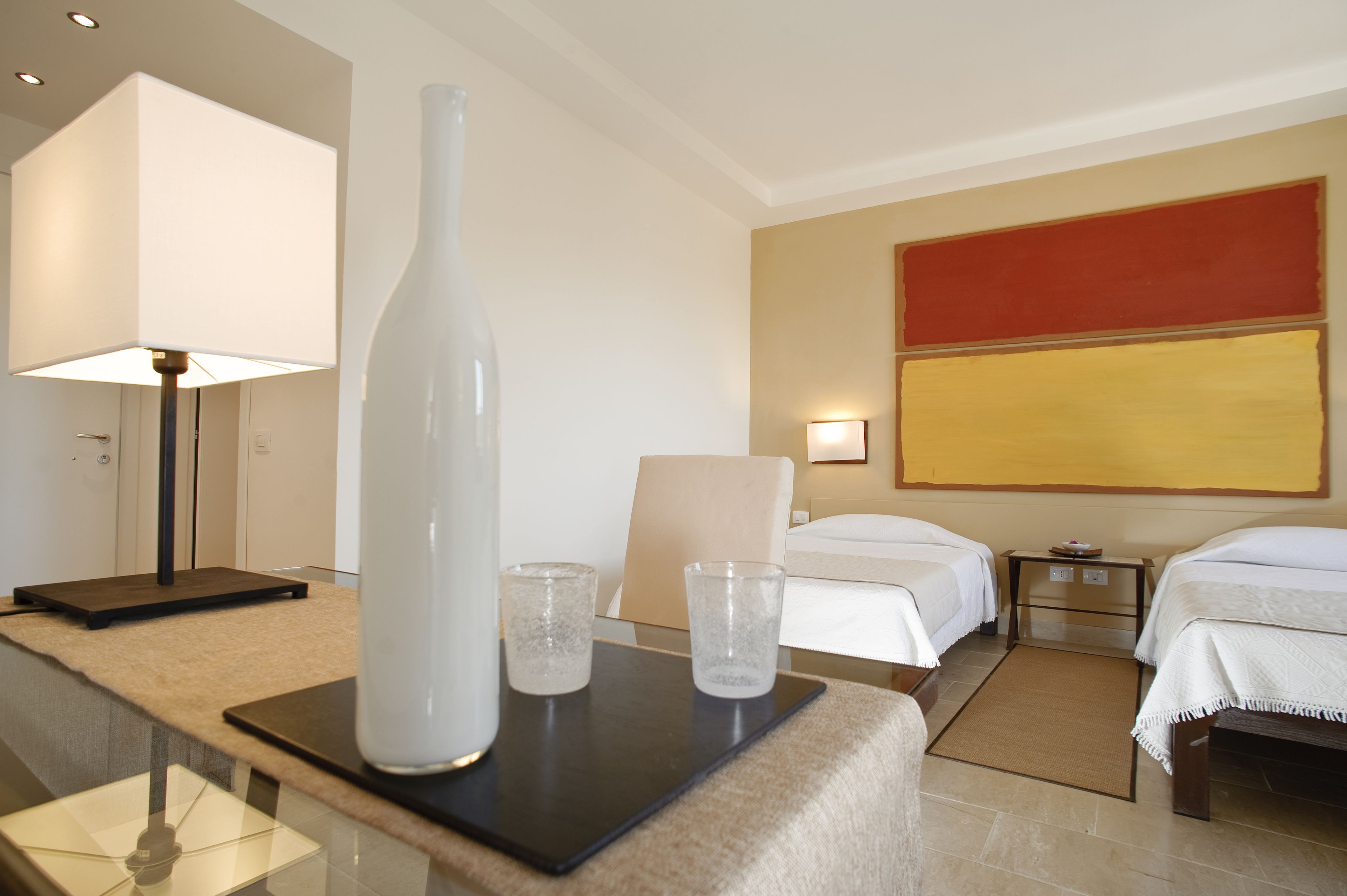 A hotel room with a desk, two beds, a large abstract painting, and a standing lamp.