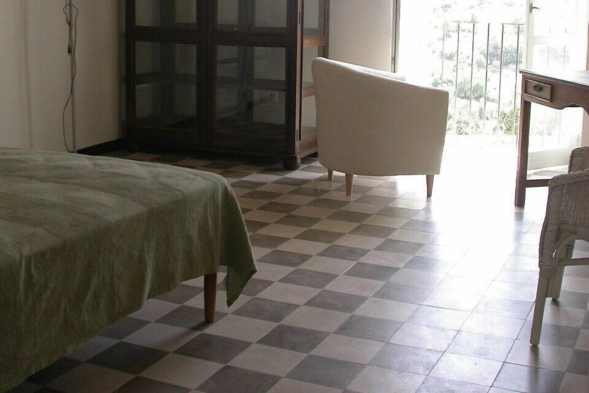 A room with a checkered floor, a bed, a cabinet, a chair, and a balcony with a railing.